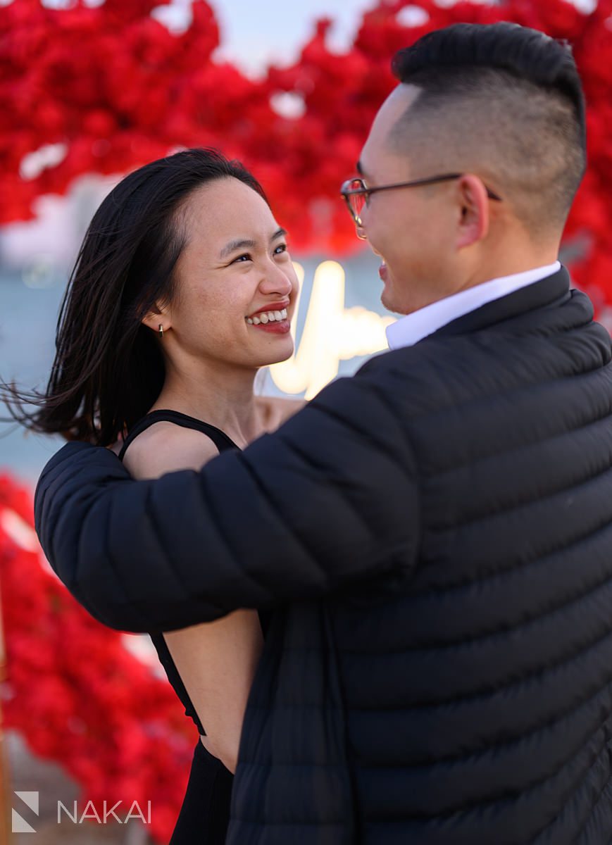 All smiles in front of flower heart wreath backdrop on North Ave Beach. Engagement proposal ideas Chicago with skyline 