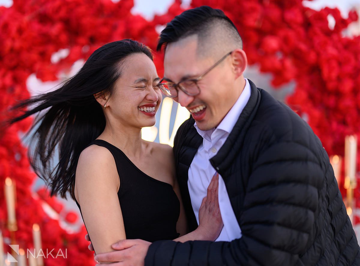 laughing in front of flower wall backdrop on North Ave Beach. Engagement proposal ideas Chicago with skyline 