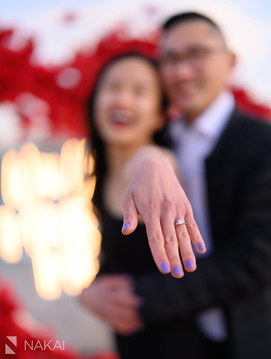 Showing the ring. Engagement proposal ideas Chicago with skyline + flower heart wreath backdrop
