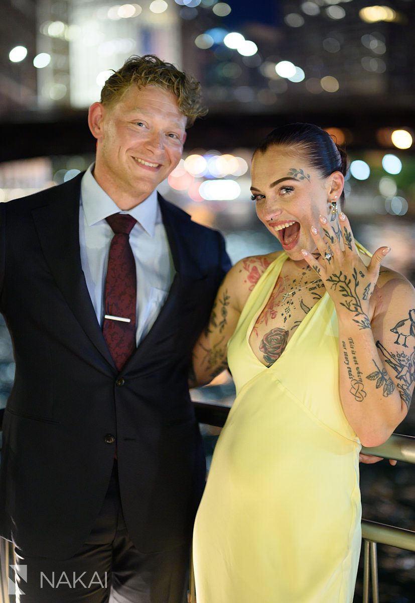holding up ring hand smiling chicago riverwalk engagement at night